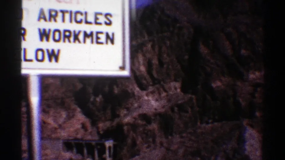 1969 Arizona home-movie frame with the dropped-articles warning sign partly blocked by a dark foreground strip.