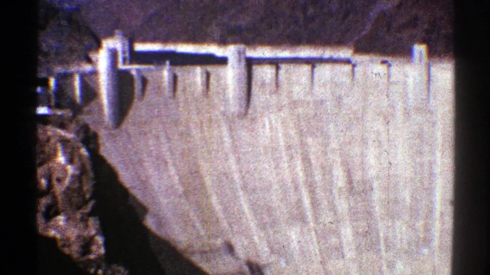 1969 Arizona 8mm frame looking down at a massive concrete dam wall set into rugged mountain terrain.