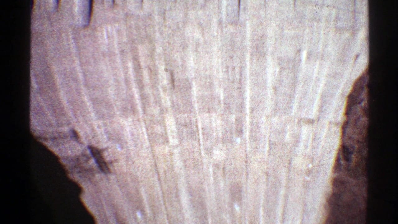 1969 8mm view of Hoover Dam's textured concrete face, framed by dark canyon shadow from a high visitor vantage point.