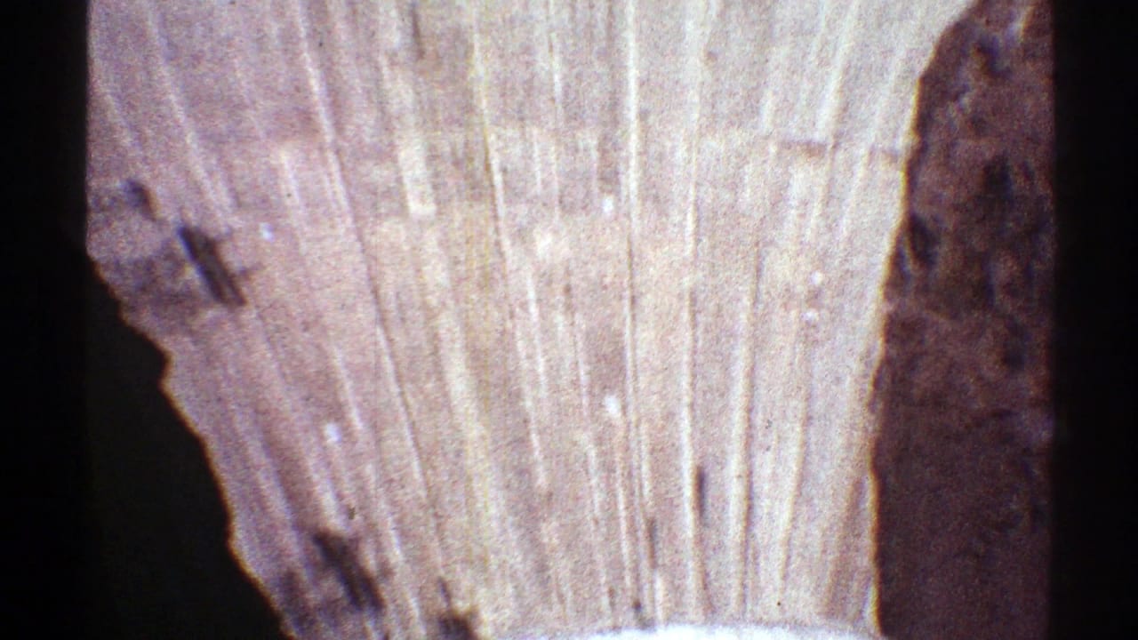 Late-1960s 8mm frame showing Hoover Dam's concrete face, vertical surface marks, and a dark canyon wall at the side.