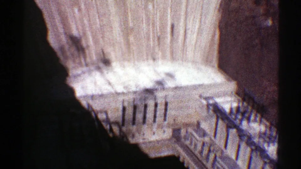 1969 Hoover Dam footage looking down toward lower platform structures, railings, and stairs at the base of the concrete wall.