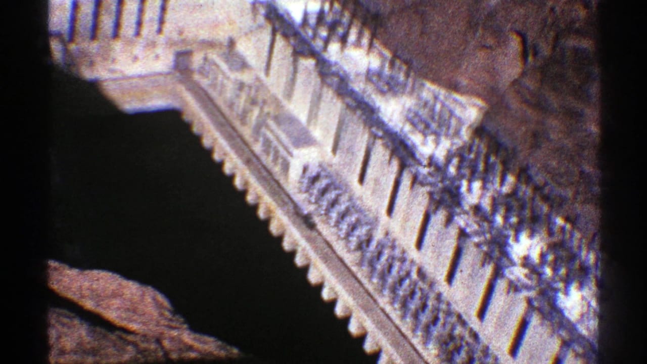 1969 Arizona 8mm frame showing a pale stepped building with railings seen from a high overlook near a rocky cliffside.