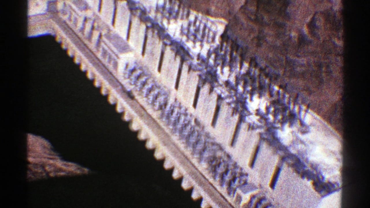 1969 Arizona travel frame looking down across a long pale building edge, rows of railings, and adjacent rugged rock.