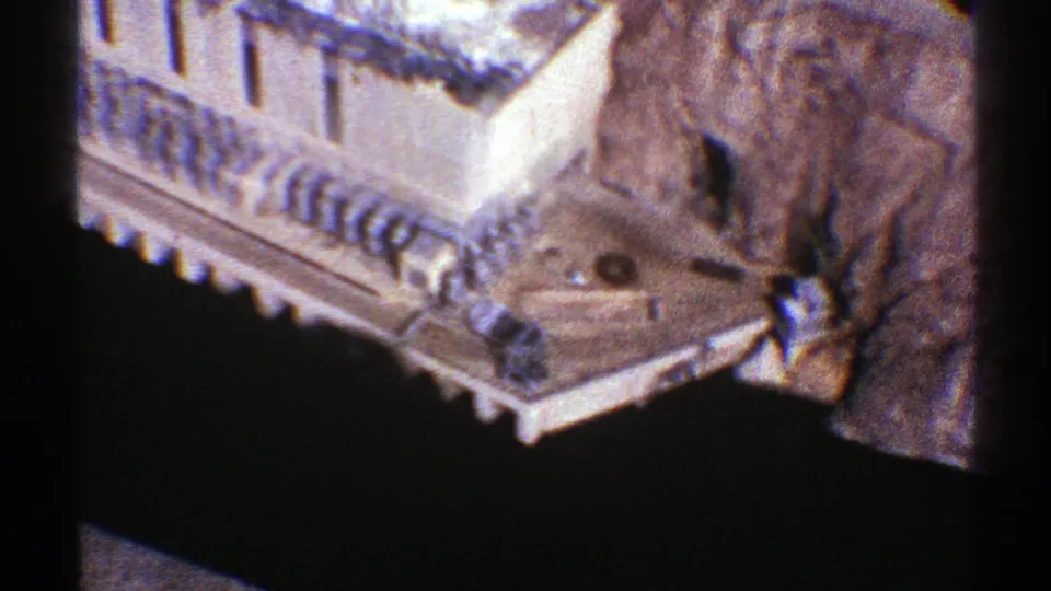 1969 Arizona frame showing a pale building corner with railings, a nearby rock face, and deep shadows from a high viewpoint.