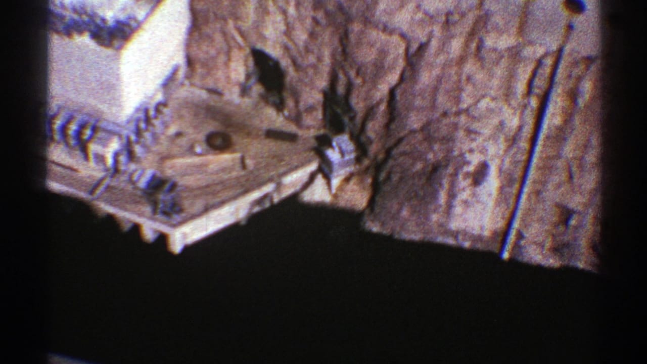 1969 Arizona 8mm aerial footage showing rough canyon rock above a dark river or reservoir, with visible film gate edges.