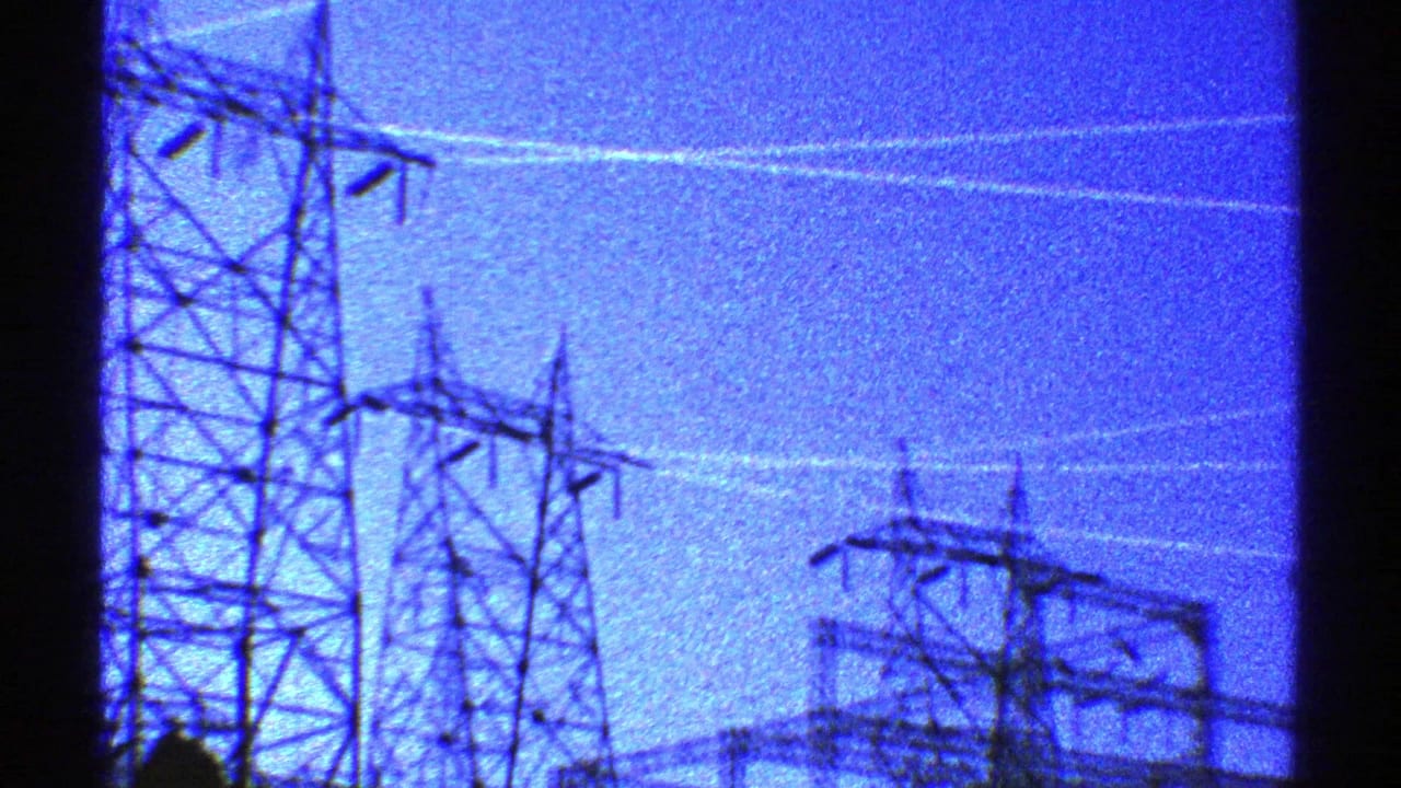 1969 Arizona 8mm frame showing lattice transmission towers and power lines silhouetted against a grainy blue dusk sky.