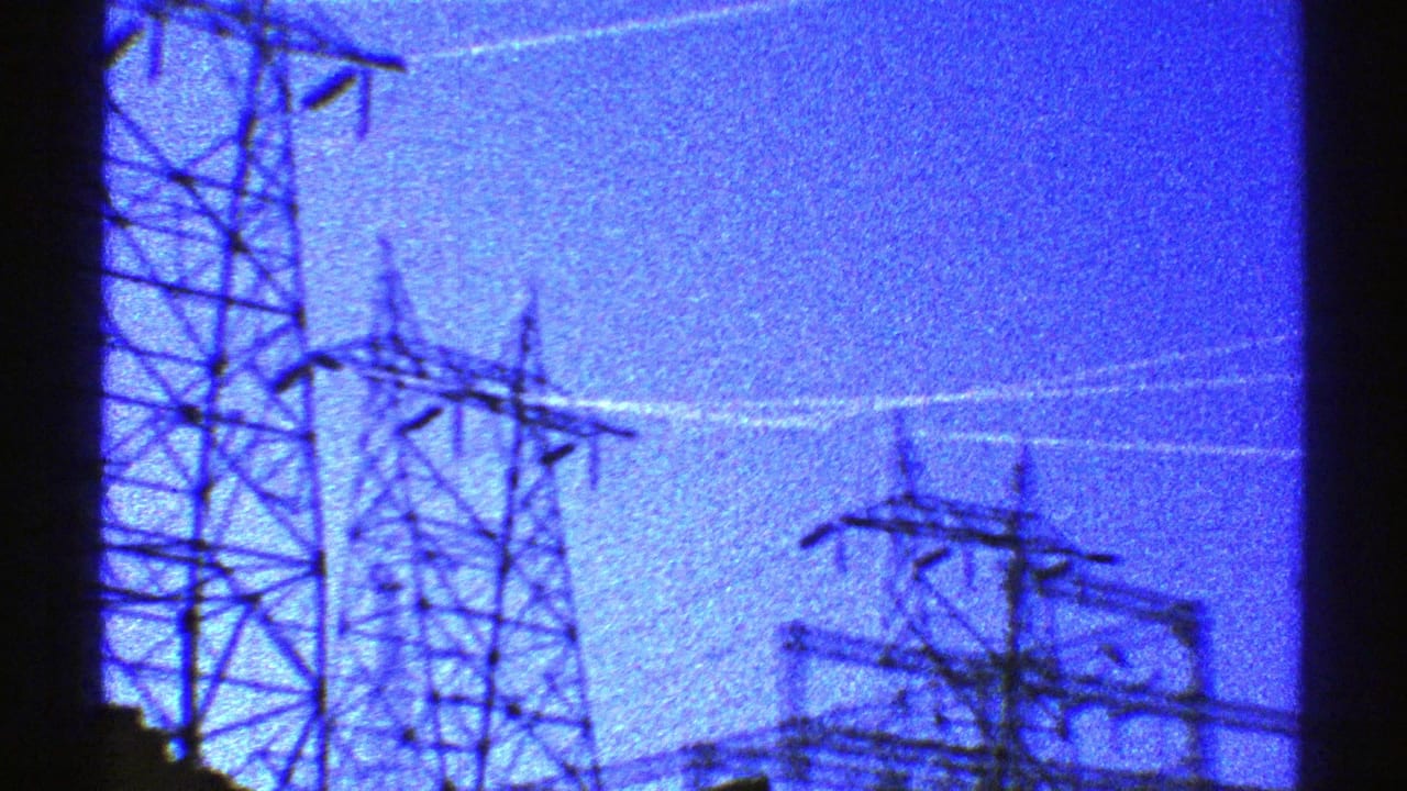 1969 Arizona home-movie frame with several electrical transmission towers crossing a blue dusk sky.