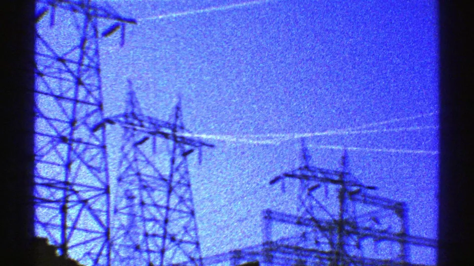 1969 Arizona home-movie frame with several electrical transmission towers crossing a blue dusk sky.