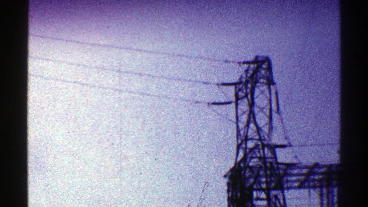 1969 Arizona 8mm frame with a tall utility tower, crossarms, and power lines against a hazy blue-purple sky.