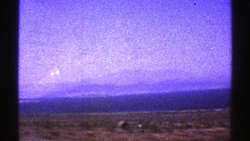 1969 Arizona 8mm frame showing open desert ground and a distant horizon under a purple-blue, grainy sky.
