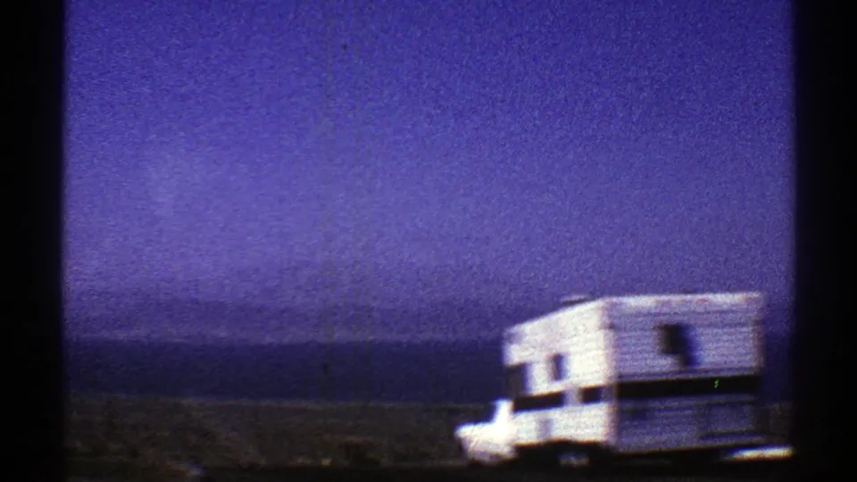 1969 Arizona 8mm frame showing a white camper vehicle near open desert land beneath a blue-purple sky.
