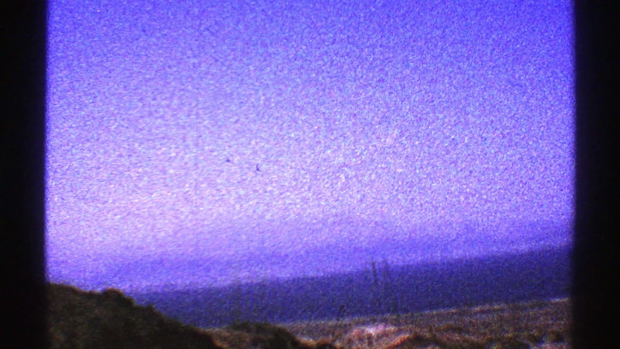 Arizona desert horizon under a purple-blue sky, with dark low terrain and heavy 8mm grain visible in the frame.