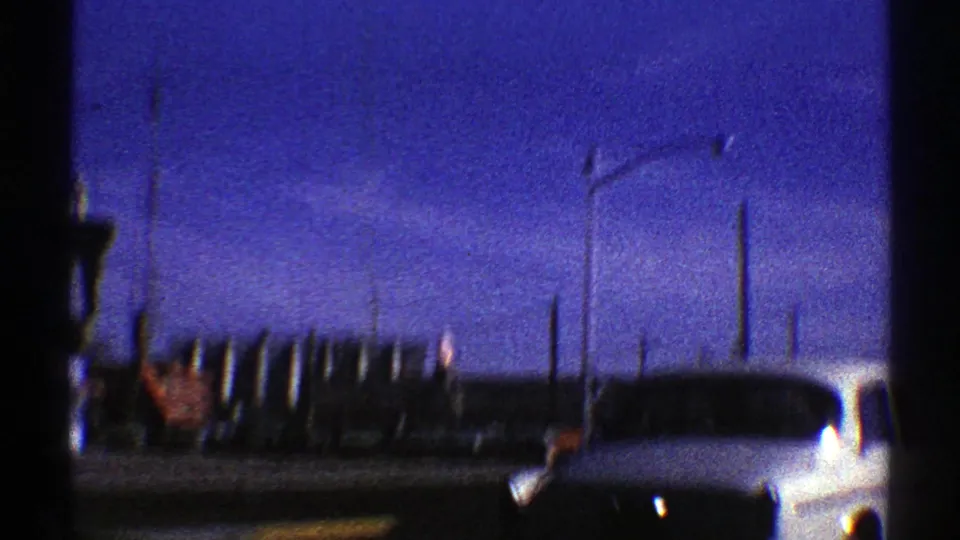 Grainy Arizona roadside view with unlit street lamps, dark vertical posts, distant terrain, and a light-colored car.