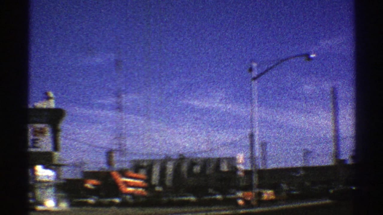 1969 Arizona 8mm frame of roadside traffic with cars, trucks, signs, streetlights, and low commercial buildings.