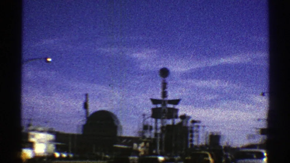 1969 Arizona urban roadside frame with a domed building, tower, cars, signs, and low structures beneath a blue sky.