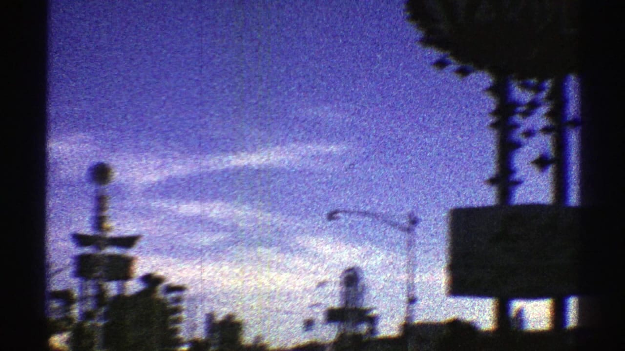 1969 8mm automobile-view footage of an Arizona city street at dusk, with traffic lights, silhouetted signs, and a purple-blue sky.