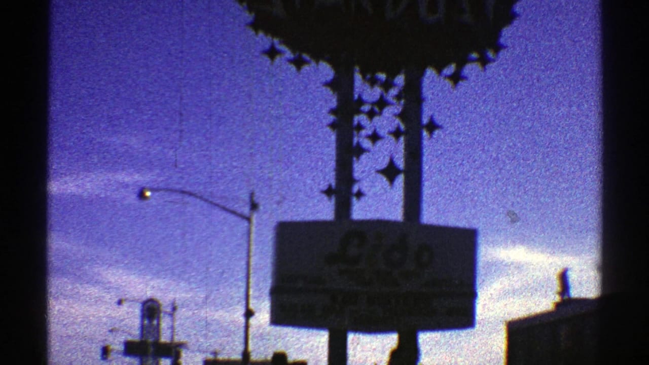 Arizona city drive frame showing a large star-adorned hotel or casino sign, a lit streetlight, and silhouetted buildings in 1969 8mm footage.