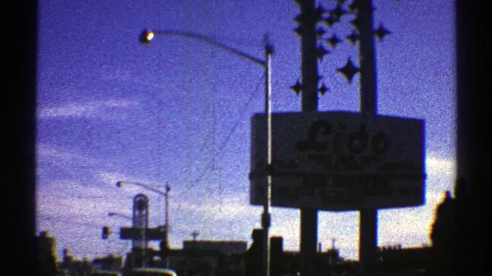 1969 Arizona home-movie frame with a prominent roadside hotel or casino sign, traffic signal, streetlight, and dark city silhouettes.