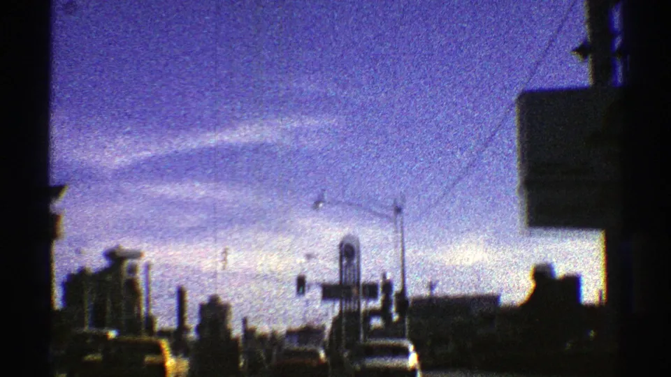 Final 1969 8mm frame from an Arizona city drive, showing vehicles, traffic lights, low buildings, and a partial roadside sign at dusk.