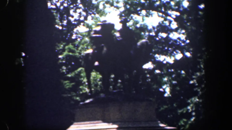 1961 Baltimore home-movie frame with a dark, tree-framed monument or statue area before the stadium view.