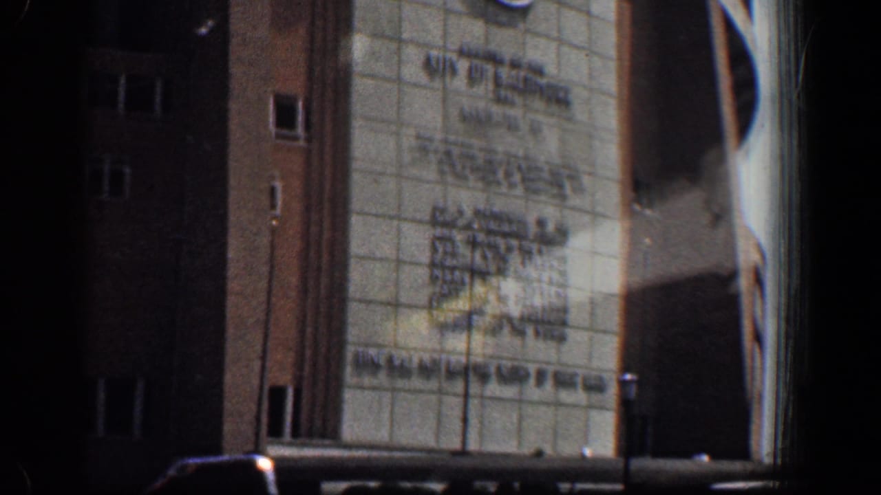 Moving car view of a large tiled and brick building facade with civic inscription.