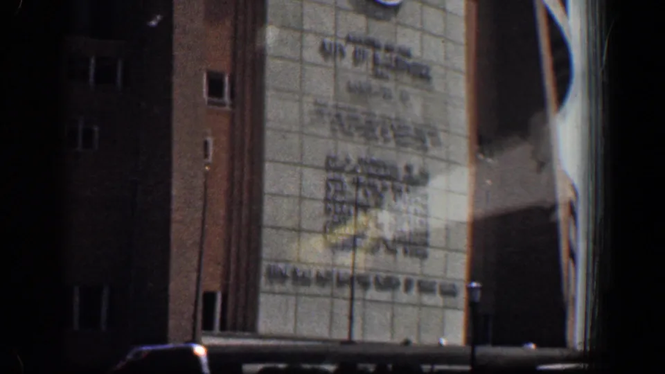 1961 Baltimore 8mm frame showing a large institutional facade with tiled wall, brick sides, street lamp, and partial car-window obstruction.
