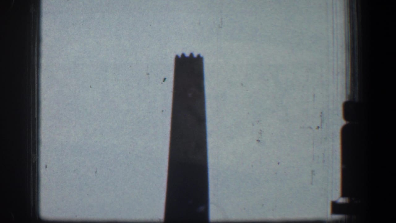 Tall smokestack silhouetted against a pale sky with dark frame edges.