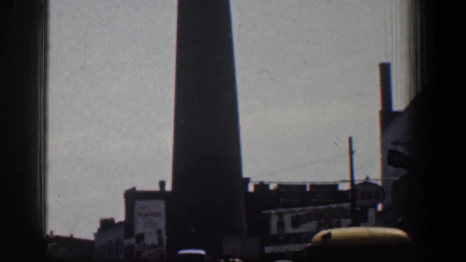 The silhouetted Baltimore smokestack stands above low industrial buildings, poles, and a rounded foreground object.