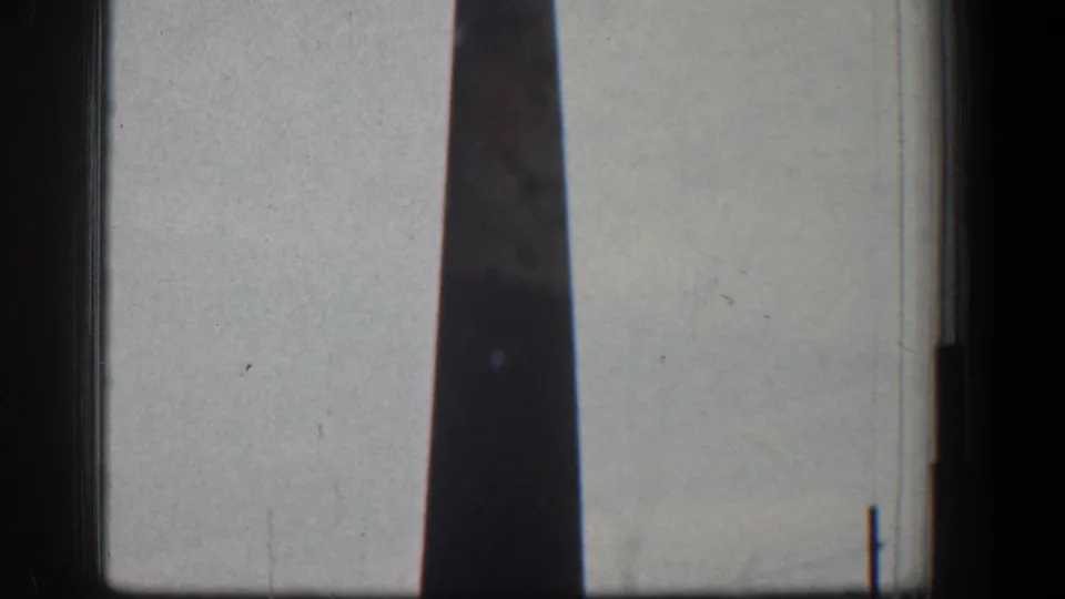 A tall narrow stack appears through dark vehicle or film framing, continuing the 1961 Baltimore industrial roadside view.