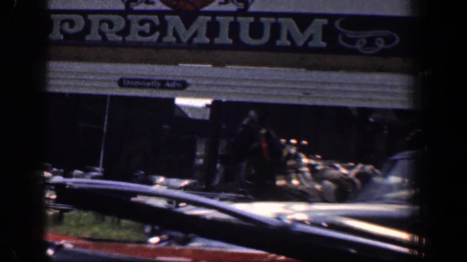 Baltimore street-view frame from 1961 showing a storefront sign reading PREMIUM, a sidewalk area, and part of a classic car roofline.