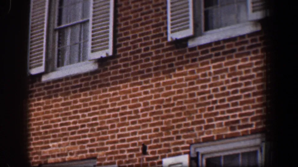 1961 Baltimore street-side view of a brick building with shuttered windows, lower window details, and a partial car at the frame edge.