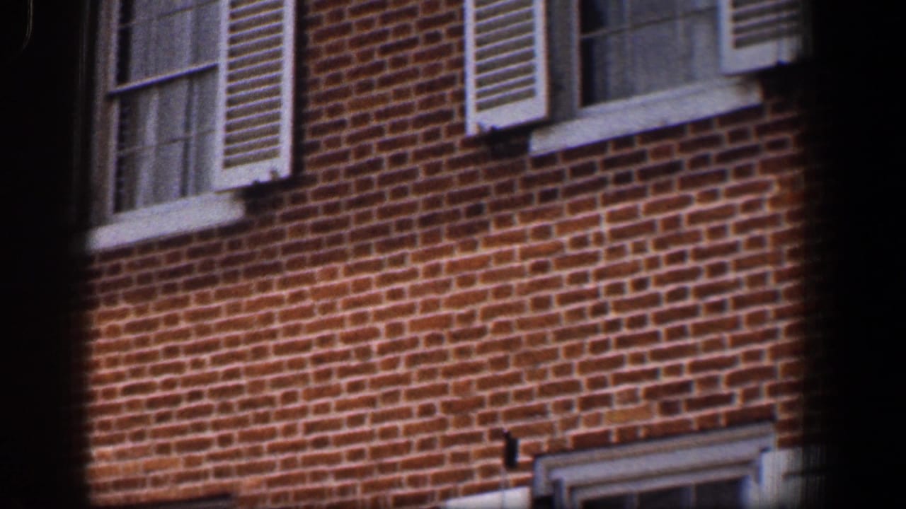 Red brick facade with white-trimmed windows and shutters, partly framed by dark film edges.