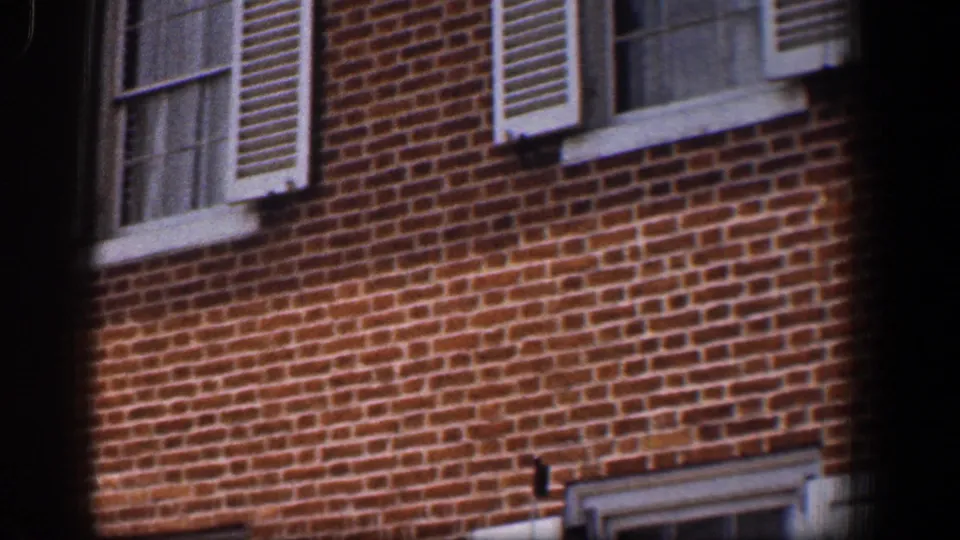 1961 Baltimore 8mm frame showing a red brick building facade with white window trim, louvered shutters, and dark vignetted edges.