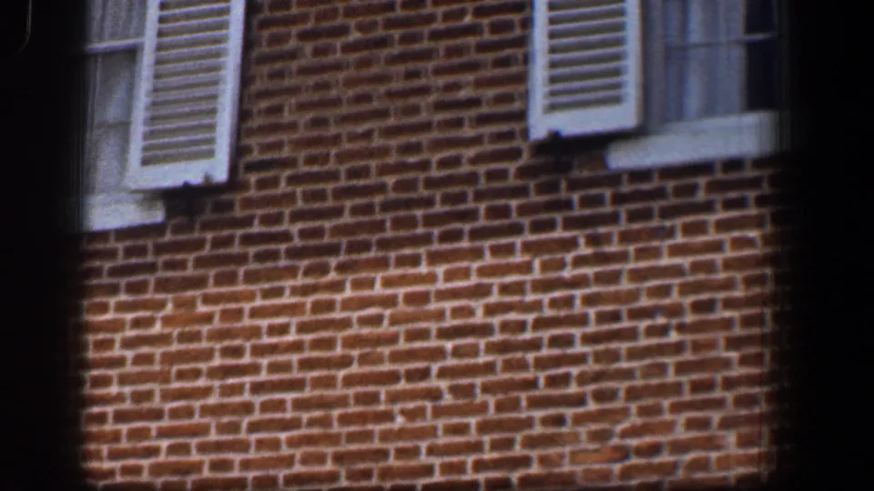 1961 Baltimore 8mm still showing red brickwork, white shutters, window trim, and a partial lower window on a close building facade.