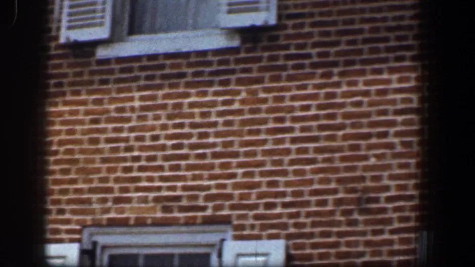 1961 Baltimore exterior frame showing a close red brick wall, cropped white shutter, window sill, and partial lower window detail.