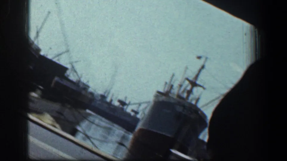 Tilted 1961 Baltimore harbor view from a moving vehicle, with ships, cranes, and water visible through the frame edge.