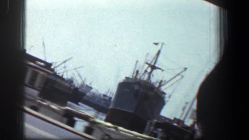 Baltimore dockyard scene with a large vessel, harbor cranes, roadway edge, and soft 8mm motion blur.
