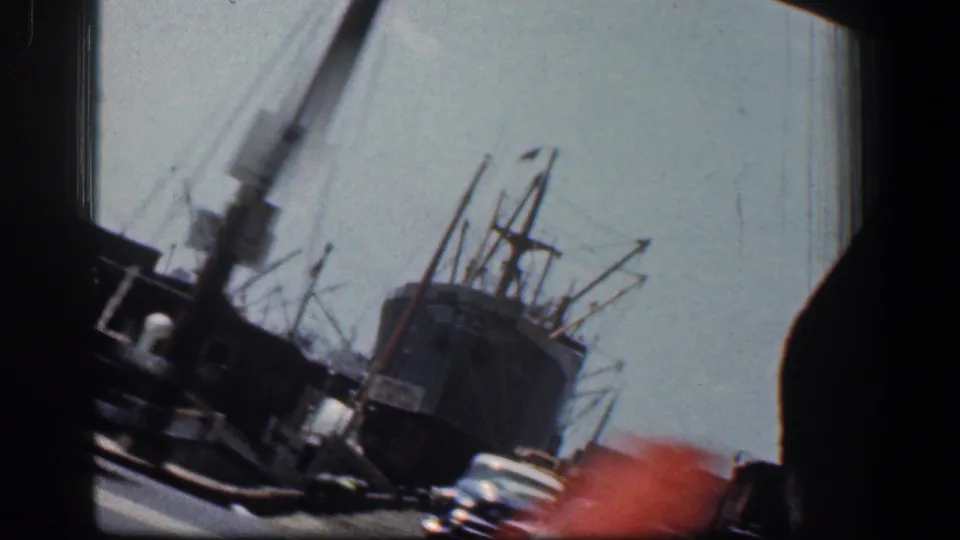 Final 1961 Baltimore dockyard frame shows a ship, cranes, roadway, and a reddish blur at the lower right edge.