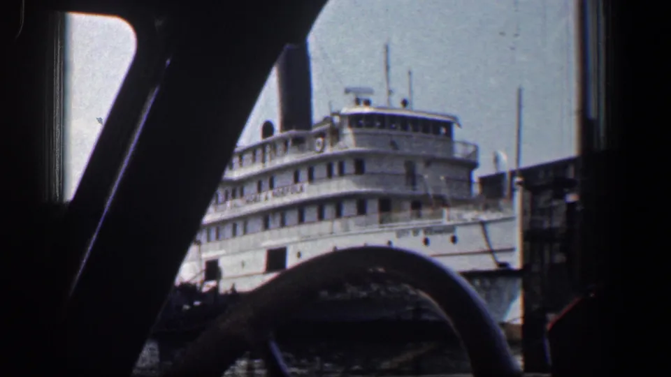 White passenger-style steamboat at a Baltimore waterfront, framed by dark windshield pillars from inside a vehicle.