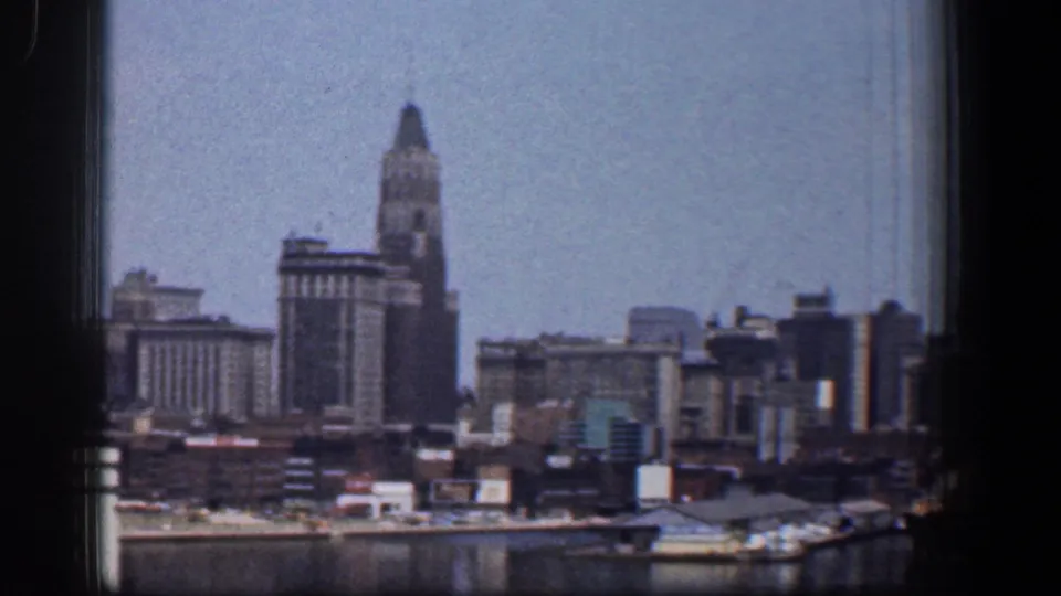 1961 Baltimore skyline seen across the waterfront, with downtown high-rises, a towered building, rooftops, and pale blue sky.