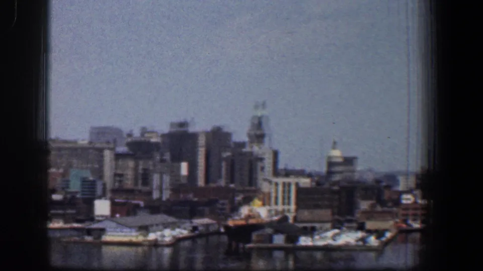 1961 Baltimore skyline and waterfront docks viewed across harbor water, with the scene partially bordered by the film frame and window edge.