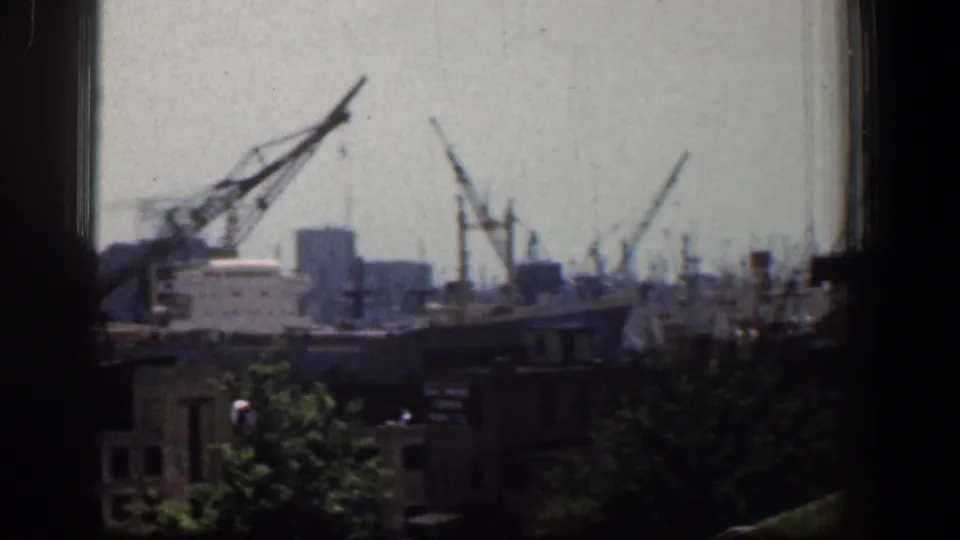 Baltimore harbor cranes and industrial structures appear beyond nearby rooftops and trees in this 1961 8mm frame.