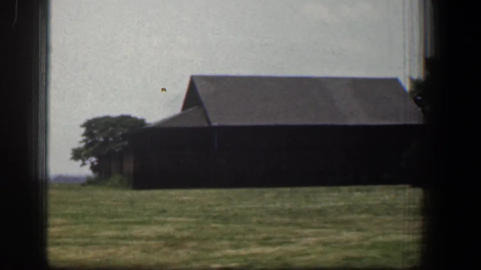 1961 Baltimore-area 8mm frame of a dark barn-like building and open grass viewed during the car journey.