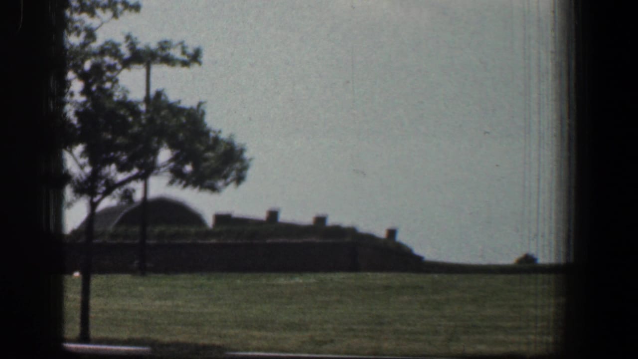 Grassy foreground with a tree, brown low building, and dark window framing.