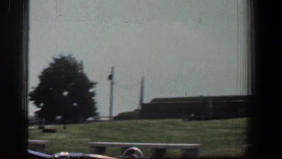 1961 Baltimore view of grassy grounds, a tree, low building, upright poles, and small bench-like structures in soft 8mm color.