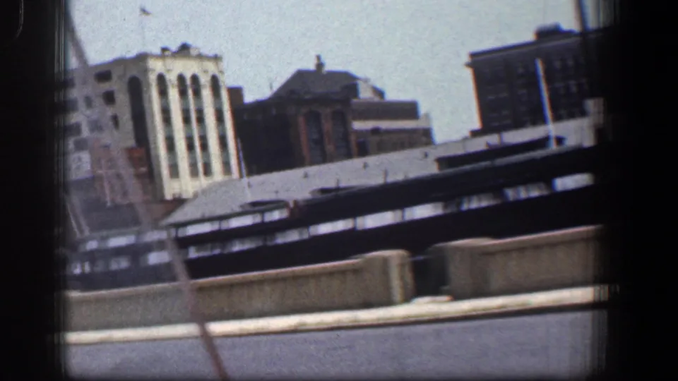 Baltimore waterfront seen from a moving vehicle, with a dark boat in front of mixed industrial buildings and 8mm frame edges.