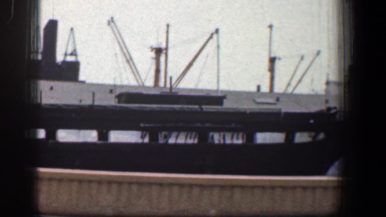 Industrial waterfront view seen through dark window framing with cranes and an elevated rail structure.