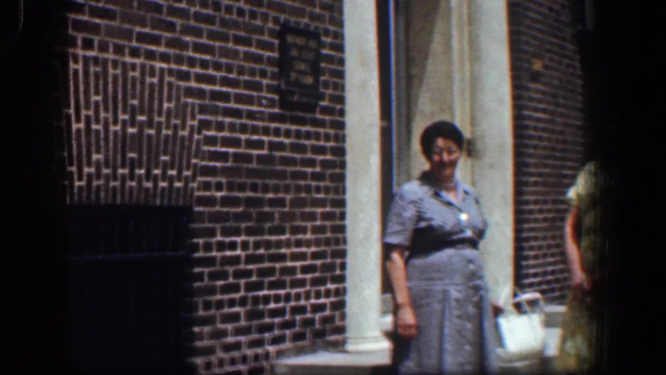 The final frame shows the woman in gray beside the Baltimore brick building entrance, with the woman in yellow partly out of frame and wall signage visible above.