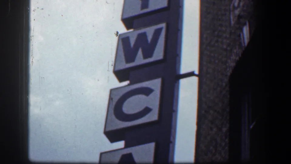 The camera frames the middle and lower letters of a vertical YWCA sign on a Baltimore building exterior.