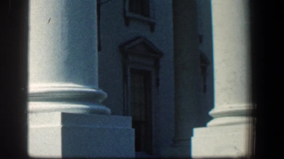 1961 Baltimore home-movie frame showing large white columns, stone bases, and a dark recessed building entrance.